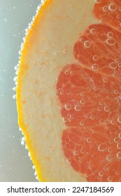 Close-up of fresh grapefruit slice on white background. Slice of red grapefruit in sparkling water on white background, close-up. Vertical image.