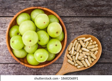 Close-up fresh organic green Amla or Indian gooseberry fruits ( phyllanthus emblica ) with capsules isolated on rustic wood table background. Overhead view. Flat lay.