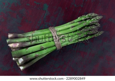 Close-up of a fresh raw asparagus bunch tied with a burlap twine on woodenbackground.