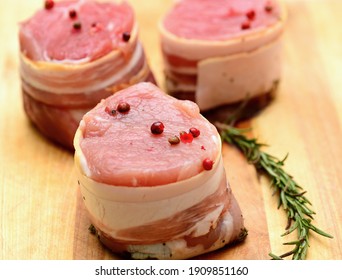 Closeup Of Fresh Raw Bacon Wrapped Pork Tenderloin Medallions Sprinkled With Whole Red Pepper And Rosemary.