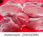 Close-up of fresh raw beef cuts displayed on a red surface, showcasing their texture and quality. Ideal for themes of meat, cooking, butcher shops, or culinary ingredients.