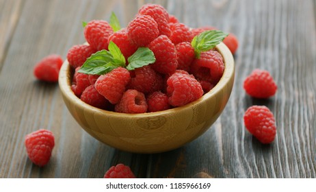 Closeup fresh red raspberry with green leaves in wooden bowl on dark table 