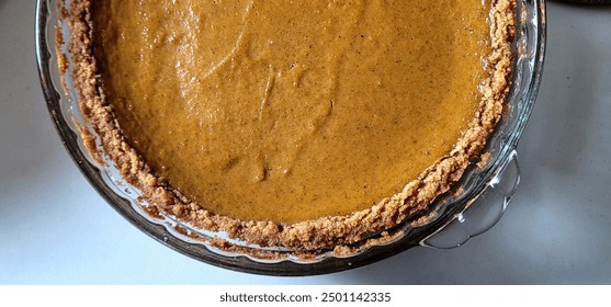 Close-up of a freshly baked homemade pumpkin pie in a glass dish, showcasing a smooth, spiced filling and a crumbly crust. Perfect for festive seasons and dessert menus. - Powered by Shutterstock