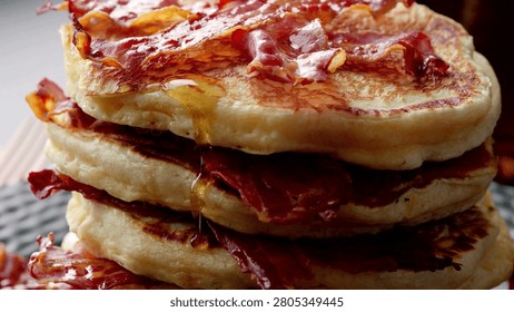 Closeup of fried bacon on a stack of delicious pancakes. Pancakes with Crispy Bacon and Maple Syrup. Person pouring syrup on fried bacon and pancakes.