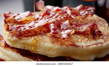Closeup of fried bacon on a stack of delicious pancakes. Pancakes with Crispy Bacon and Maple Syrup. Person pouring syrup on fried bacon and pancakes.