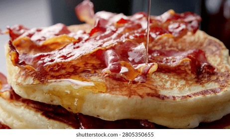 Closeup of fried bacon on a stack of delicious pancakes. Pancakes with Crispy Bacon and Maple Syrup. Person pouring syrup on fried bacon and pancakes.