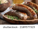 Closeup of fried bratwurst garnished with thyme on a plate on a rustic wooden table