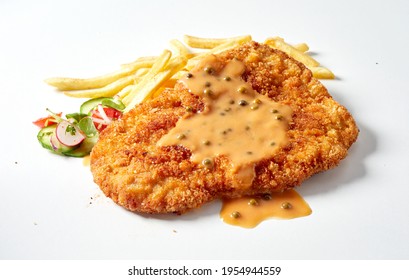 Closeup of fried breaded meat schnitzel with mustard sauce served with French fries and salad on white background