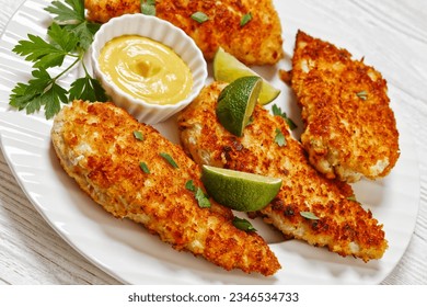 close-up of fried chicken cutlets under breadcrumbs and parmesan cheese crust on white plate with mustard and lime