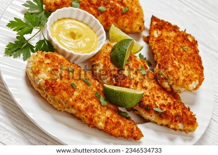 close-up of fried chicken cutlets under breadcrumbs and parmesan cheese crust on white plate with mustard and lime