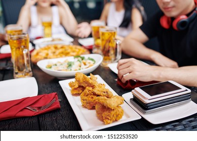 Close-up Of Fried Chicken And Mobile Phones Are On The Wooden Table With People Having Dinner In The Background In Cafe