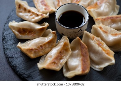 Close-up of fried japanese gyoza dumplings with soy sauce on a stone slate tray, selective focus