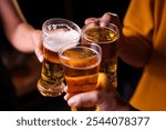 Close-up of friends clinking glasses of beer, celebrating together at a bar.The lively atmosphere captures laughter, camaraderie,good times, as young friends enjoy a night out with refreshing drinks