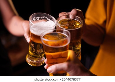 Close-up of friends clinking glasses of beer, celebrating together at a bar.The lively atmosphere captures laughter, camaraderie,good times, as young friends enjoy a night out with refreshing drinks - Powered by Shutterstock