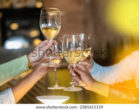A close-up of friends raising their glasses in a toast, celebrating with chilled white wine. The golden hue from the ambiance emphasizes the warmth of the gathering.