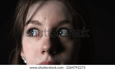 Close-up of frightened eyes of a young woman on a black background