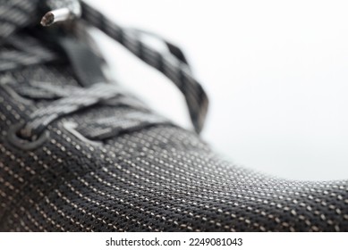 Closeup of the front of a black athletic sneaker. Selective focus on mesh texture with blurred shoelaces in the background.