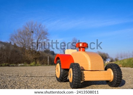 Close-up of front of Brown wooden tractor with red steering wheel, toy tractor on German asphalt road in winter in sunshine