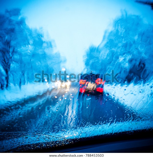closeup of\
front car window with raindrops and blurred heavy traffic during\
rush hour in winter with blue colour\
shade