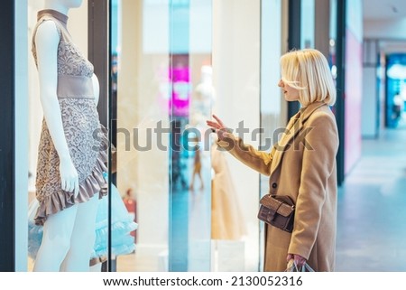 Closeup front of a late 20's woman choosing some clothes at a shopping mall. She's walking by the stores and making some choices. Photo of happy young woman on a shopping pursuit.