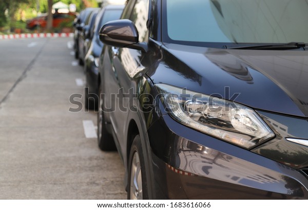 Closeup of front side of\
black car with  other cars parking in parking area beside the\
street in sunny day.