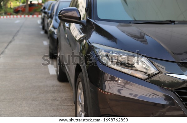 Closeup of front side of\
black car with  other cars parking in parking area beside the\
street in sunny day.