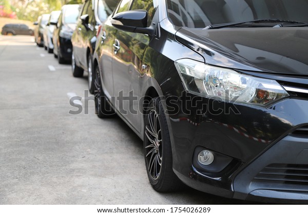 Closeup of\
front side of black car with  other cars parking in outdoor parking\
area beside the street in sunny\
day.