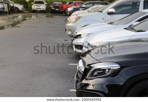 Closeup of\
front side of black car with other cars parking in outdoor parking\
area in twilight evening of rainy\
day.