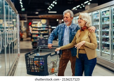 Closeup Front View Of Early 60's Couple Walking Through Supermarket Aisle And Picking Some Healthy Products.