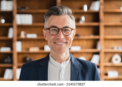 Closeup front view portrait of handsome mature middle-aged caucasian businessman freelancer bank employee in formal suit and glasses looking at camera in office at work place
