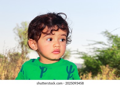 Close-up front view portrait of An Indian cute little cute male boy child posing outside and blur background of green nature outdoors