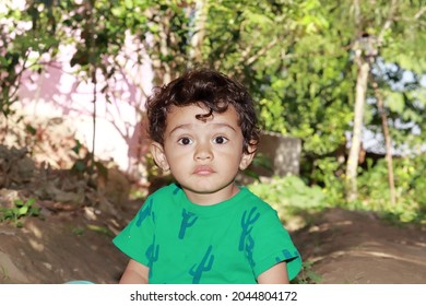 Close-up Front View Portrait Photo Of A Cute Little Cute Hindu Indian Community Child Standing In The Garden Looking At The Camera And Wearing A Green Shirt