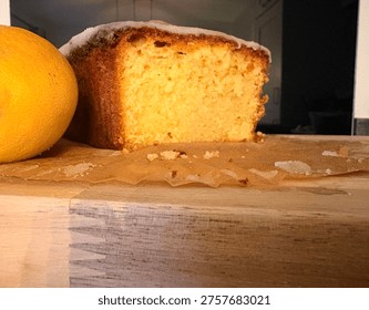 Close-Up Front View Of Sliced Lemon Loaf Cake On Wooden Board With Black Kitchen Backsplash. 