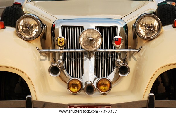 Close-up of the front of a vintage
automobile showing the grill, horns, headlights,
etc.