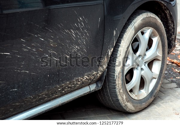 Close-up of a front wheel of a\
dirty car with a fender and a door dirtied with splashes of\
dirt.