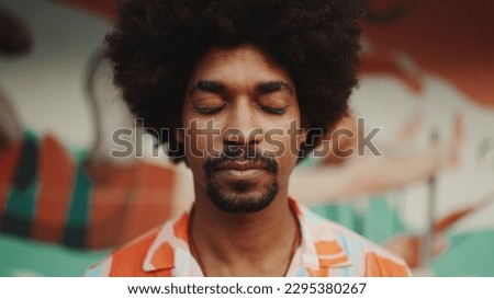 Close-up frontal portrait of  young man opens his eyes looks at the camera and smiling standing on urban street background. Urban lifestile