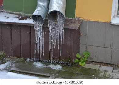 Close-up Of Frozen Drainpipe. Drain Pipe With Frozen Stream Of Water Near House Brick Wall