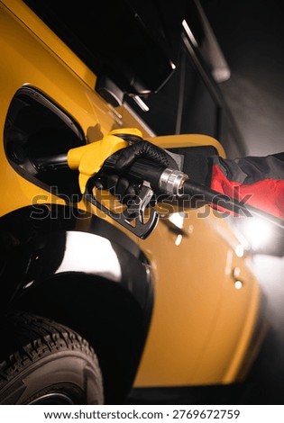 Close-up of fuel nozzle inserted into car tank. Refueling process, automotive energy, transportation and fuel service concept with dramatic lighting.