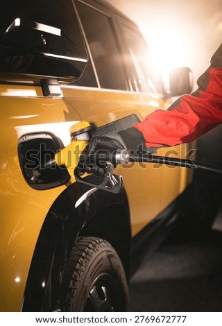 Close-up of fuel nozzle inserted into car tank. Refueling process, automotive energy, transportation and fuel service concept with dramatic lighting.