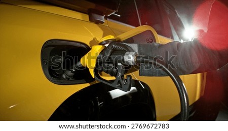 Close-up of fuel nozzle inserted into car tank. Refueling process, automotive energy, transportation and fuel service concept with dramatic lighting.