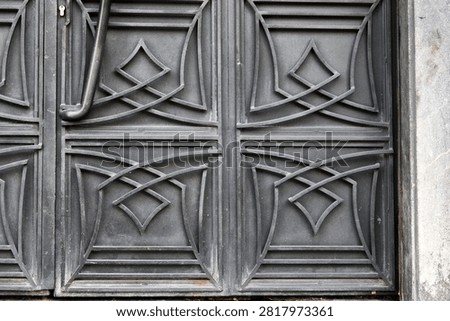 Close-up full frame view of a heavy black wrought iron metal door featuring elegant geometric Art Deco style embossed patterns and line ornamentation.