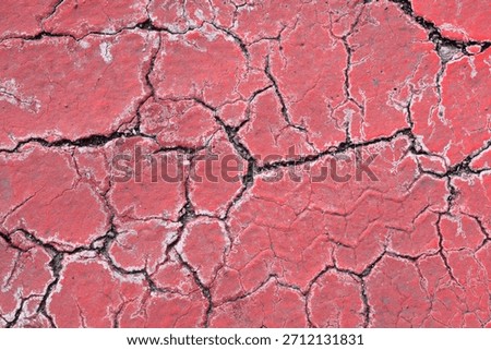 A close-up, full-frame abstract background of a rough red cracked surface showing deep fissures and a faint textured tire track impression