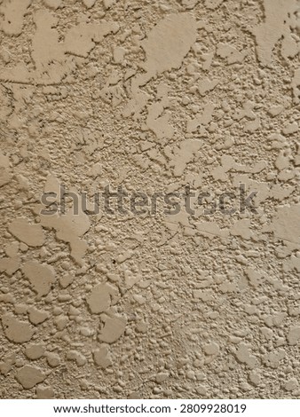 Close-up full-frame texture of a rough, uneven beige stucco wall featuring a heavy knockdown plaster pattern.