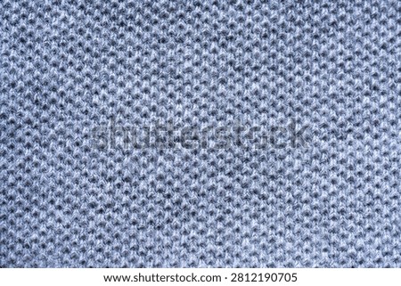 A close-up, full-frame view of a grey knitted fabric. The texture of the fabric is clearly visible, showing the interlinked loops of yarn.