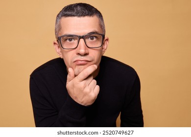 Closeup of funny pensive male wearing jumper and glasses deep in contemplation with quizzical face brainstorming ideas and strategies while experiencing uncertainty isolated over beige background - Powered by Shutterstock