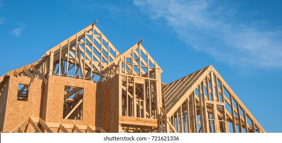 Close-up of gables roof on stick built home under construction and blue sky in Humble, Texas, USA. New build roof with wooden truss, post and beam framework. Timber frame house, real estate. Panorama