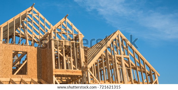 Close-up of gables roof on stick built home\
under construction and blue sky in Humble, Texas, USA. New build\
roof with wooden truss, post and beam framework. Timber frame\
house, real estate.\
Panorama
