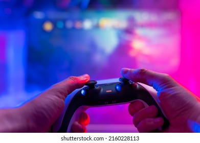 Close-up. Gamepad in the hands of a gamer. Plays video games on the big screen TV. Neon lighting. Video games, communications, cyberspace, eSports, youth culture. - Shutterstock ID 2160228113