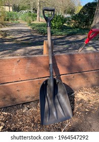 Close-up Of Garden Shovel Leaning Against Wood Fence In Community Garden