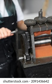 Close-up Of Gears Of Roll Press. Rolling Silver. Jewelry Repair Shop. Woman Is Out Of Focus In Background.